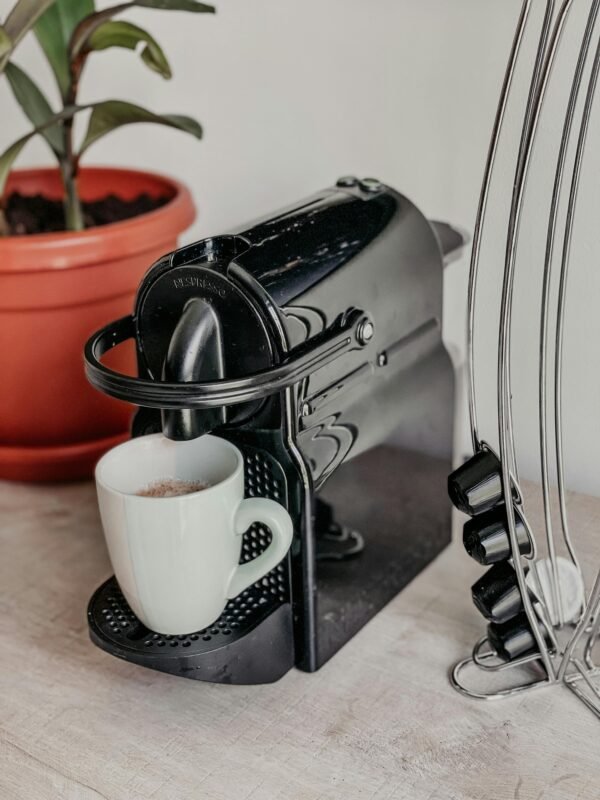 A modern black coffee maker with a white cup and a potted plant nearby, perfect for a cozy kitchen setup.